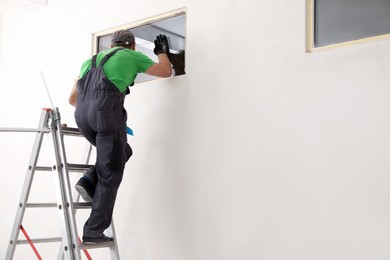 Worker in uniform installing double glazing window indoors