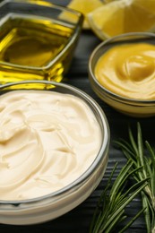 Photo of Glass bowl with fresh mayonnaise and ingredients on black wooden table, closeup