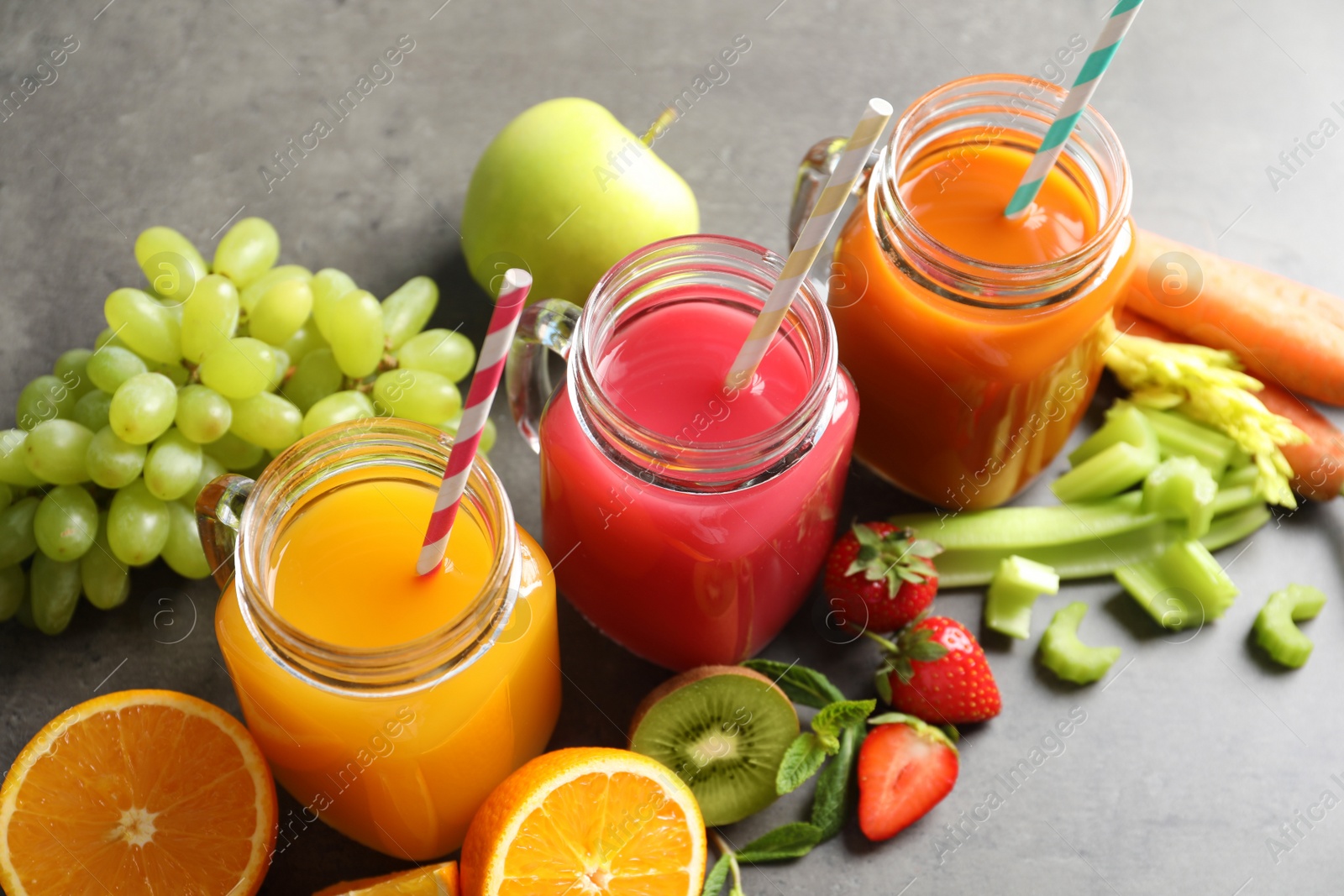 Photo of Mason jars with different juices and fresh ingredients on table