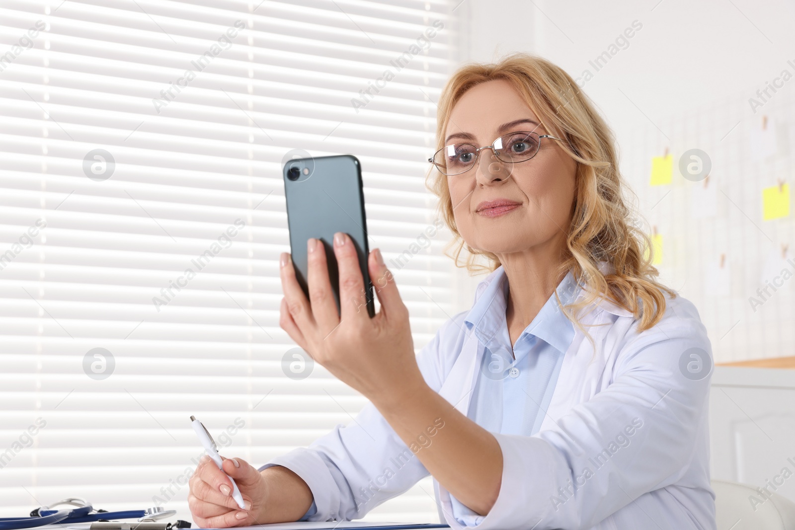 Photo of Doctor with glasses and smartphone consulting patient in clinic. Online medicine concept