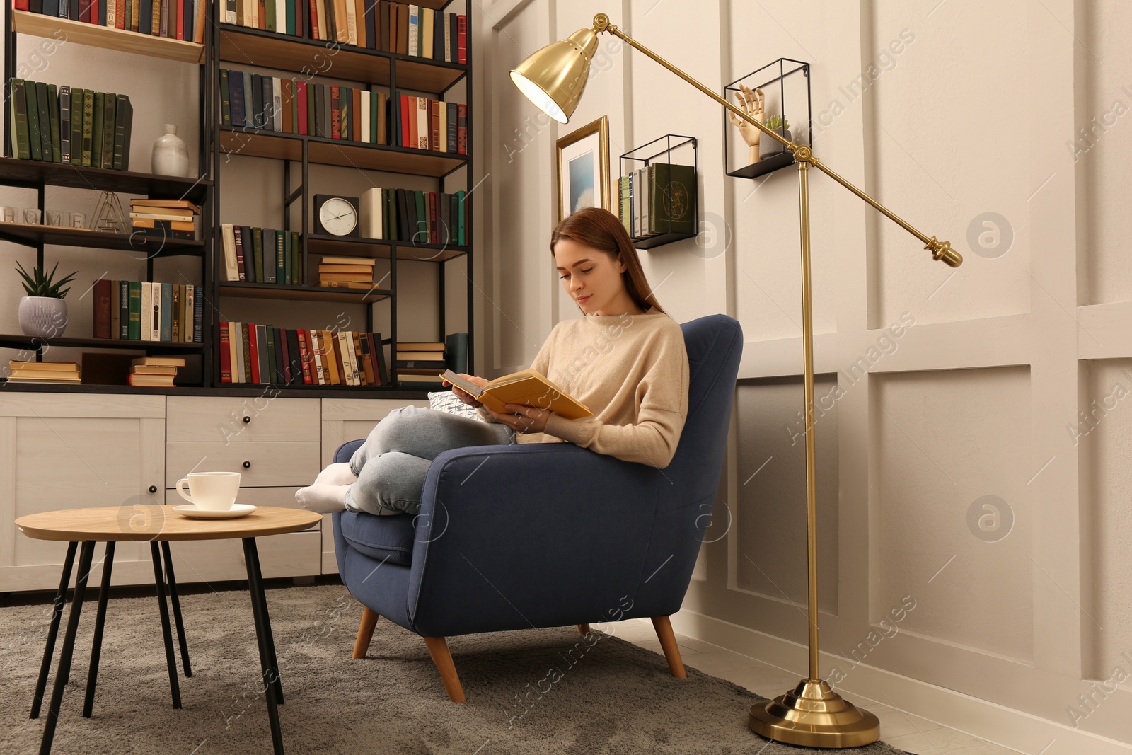 Photo of Young woman reading book in armchair indoors. Home library