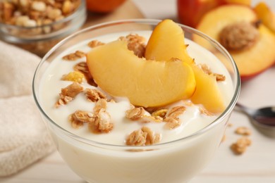 Photo of Tasty peach yogurt with granola and pieces of fruit in dessert bowl on table, closeup