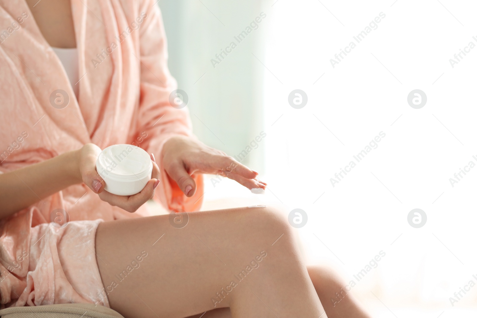 Photo of Young woman with jar of body cream at home