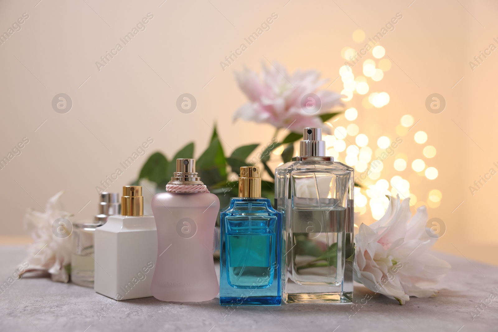 Photo of Perfume bottles and bouquet of beautiful lily flowers on table against beige background with blurred lights, closeup