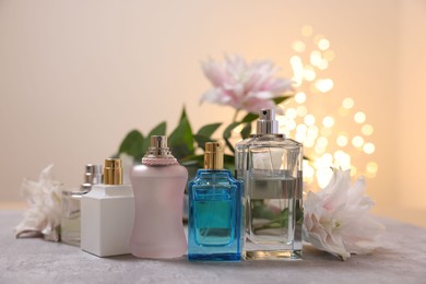 Perfume bottles and bouquet of beautiful lily flowers on table against beige background with blurred lights, closeup