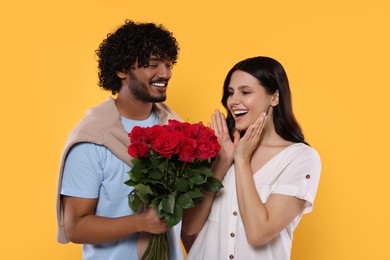 Photo of International dating. Handsome man presenting roses to his beloved woman on yellow background
