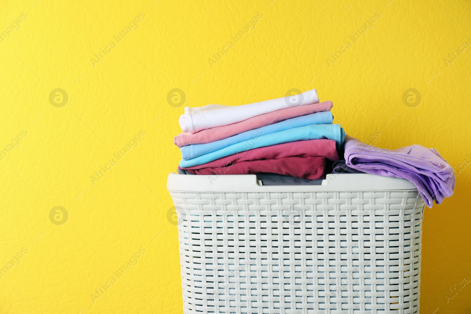 Photo of Basket with clean laundry on yellow background, space for text