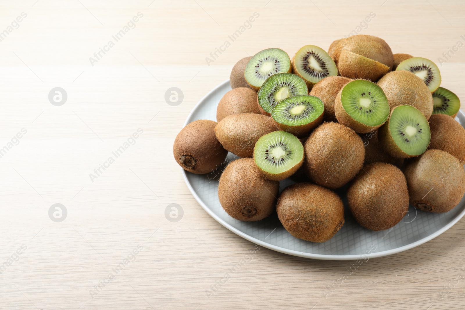 Photo of Fresh ripe kiwis on light wooden table, space for text