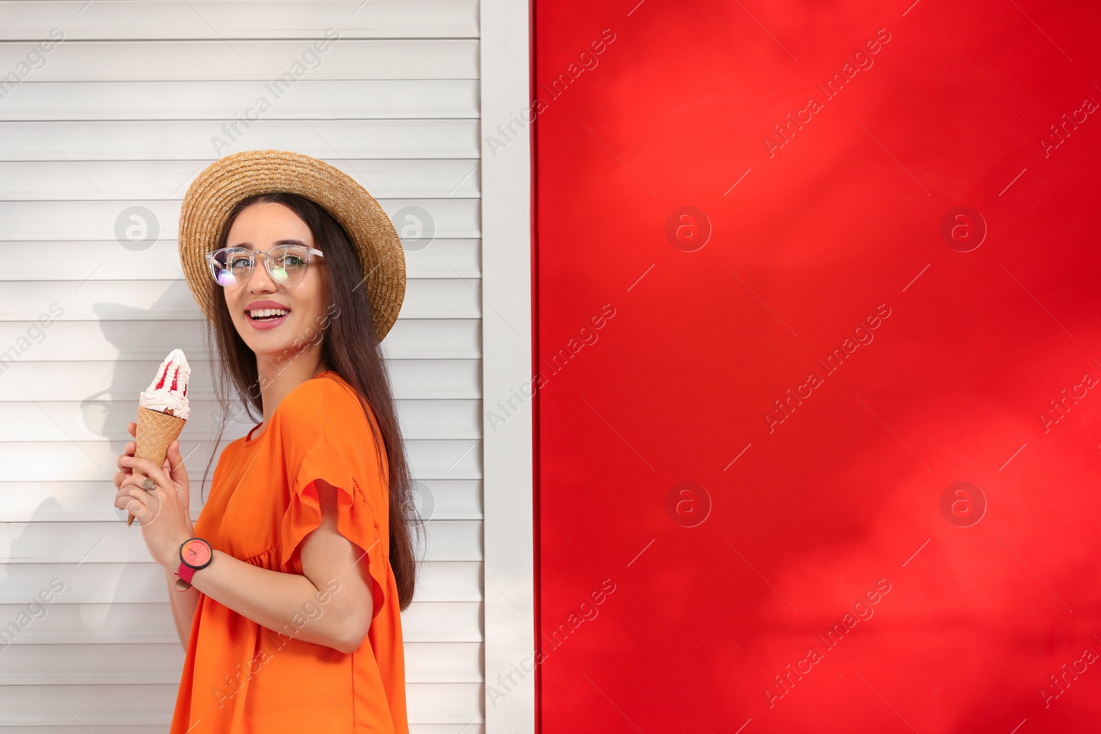 Photo of Happy young woman with delicious ice cream in waffle cone near color wall. Space for text