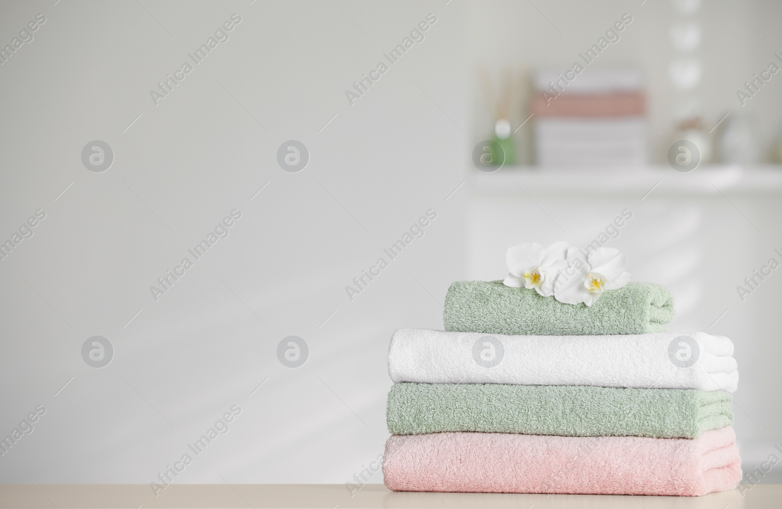 Photo of Stack of clean soft towels with orchid flowers on white table indoors. Space for text