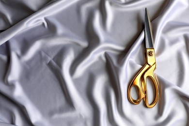 Photo of Scissors on silk fabric, top view. Space for text