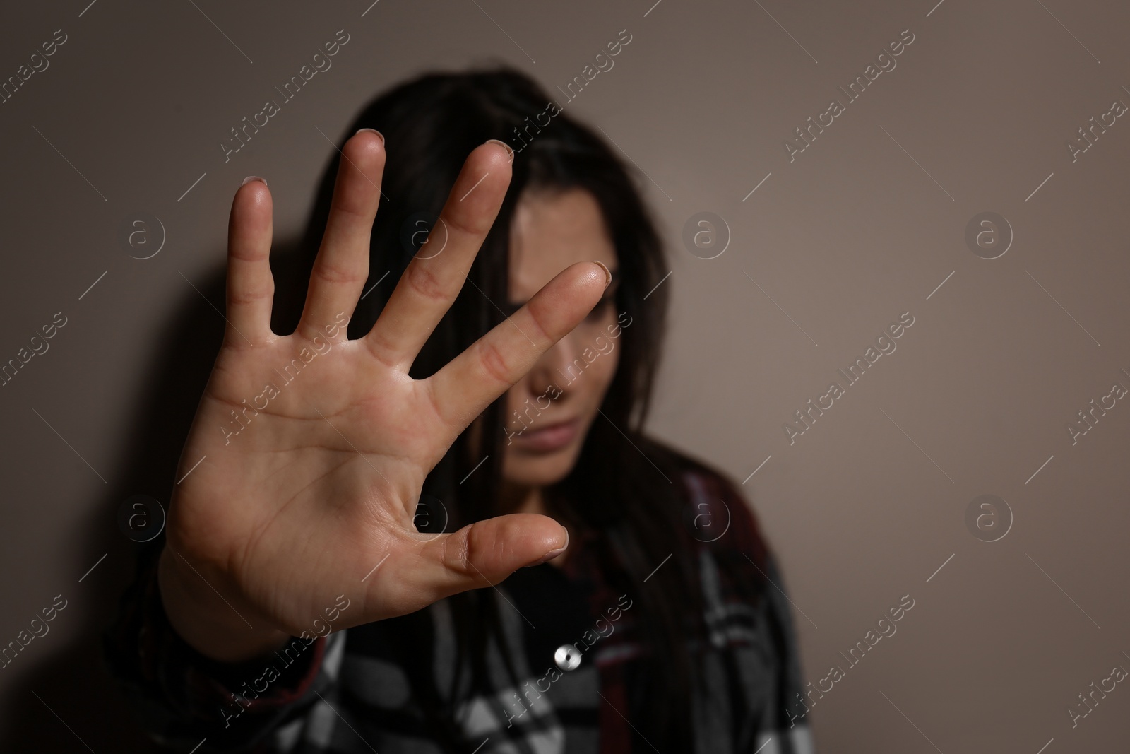 Photo of Abused young woman making stop gesture near beige wall, focus on hand. Domestic violence concept