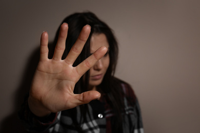 Photo of Abused young woman making stop gesture near beige wall, focus on hand. Domestic violence concept