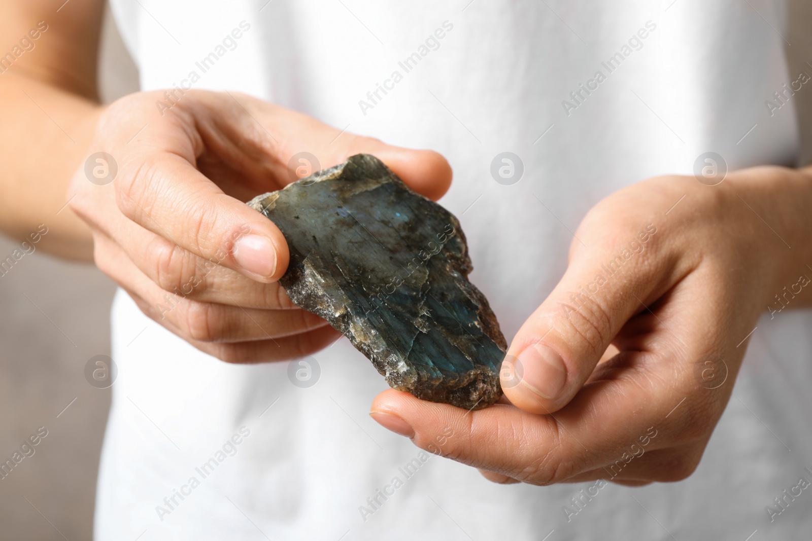 Photo of Young woman holding beautiful labradorite gemstone on beige background, closeup