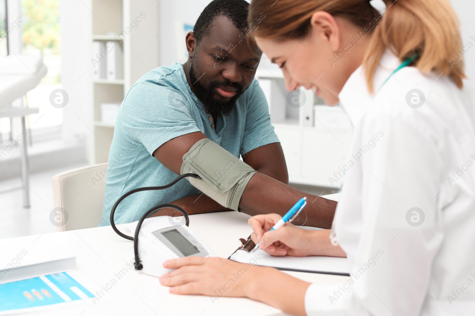 Photo of Young doctor checking African-American patient's blood pressure in hospital