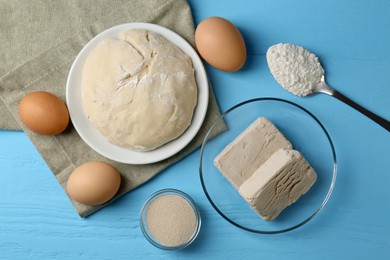 Photo of Different types of yeast, eggs, dough and flour on light blue wooden table, flat lay