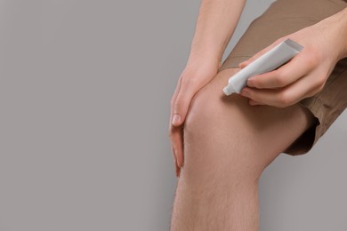 Photo of Man applying ointment from tube onto his knee on light grey background, closeup. Space for text