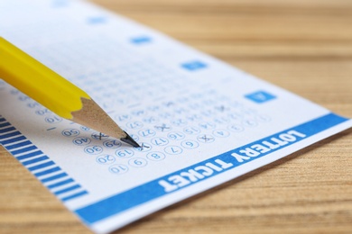 Photo of Filling out lottery ticket with pencil on wooden table, closeup. Space for text