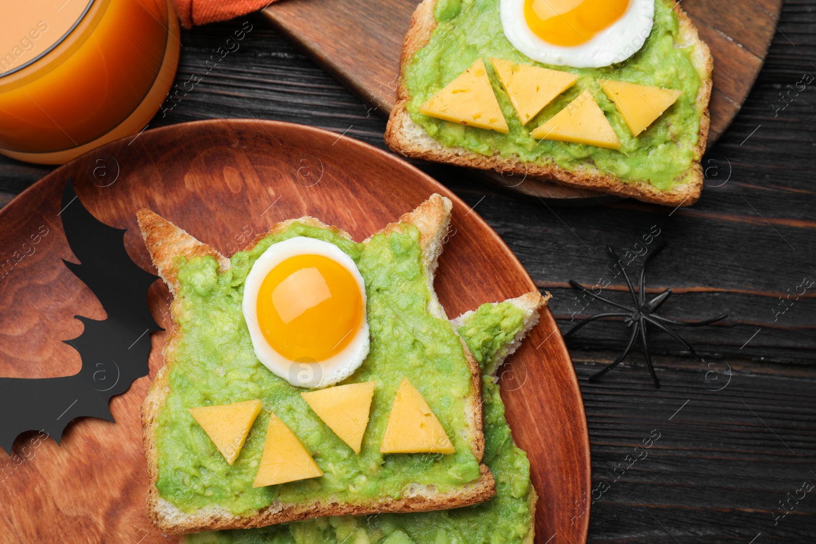 Photo of Halloween themed breakfast served on black wooden table, flat lay. Tasty sandwiches with fried eggs