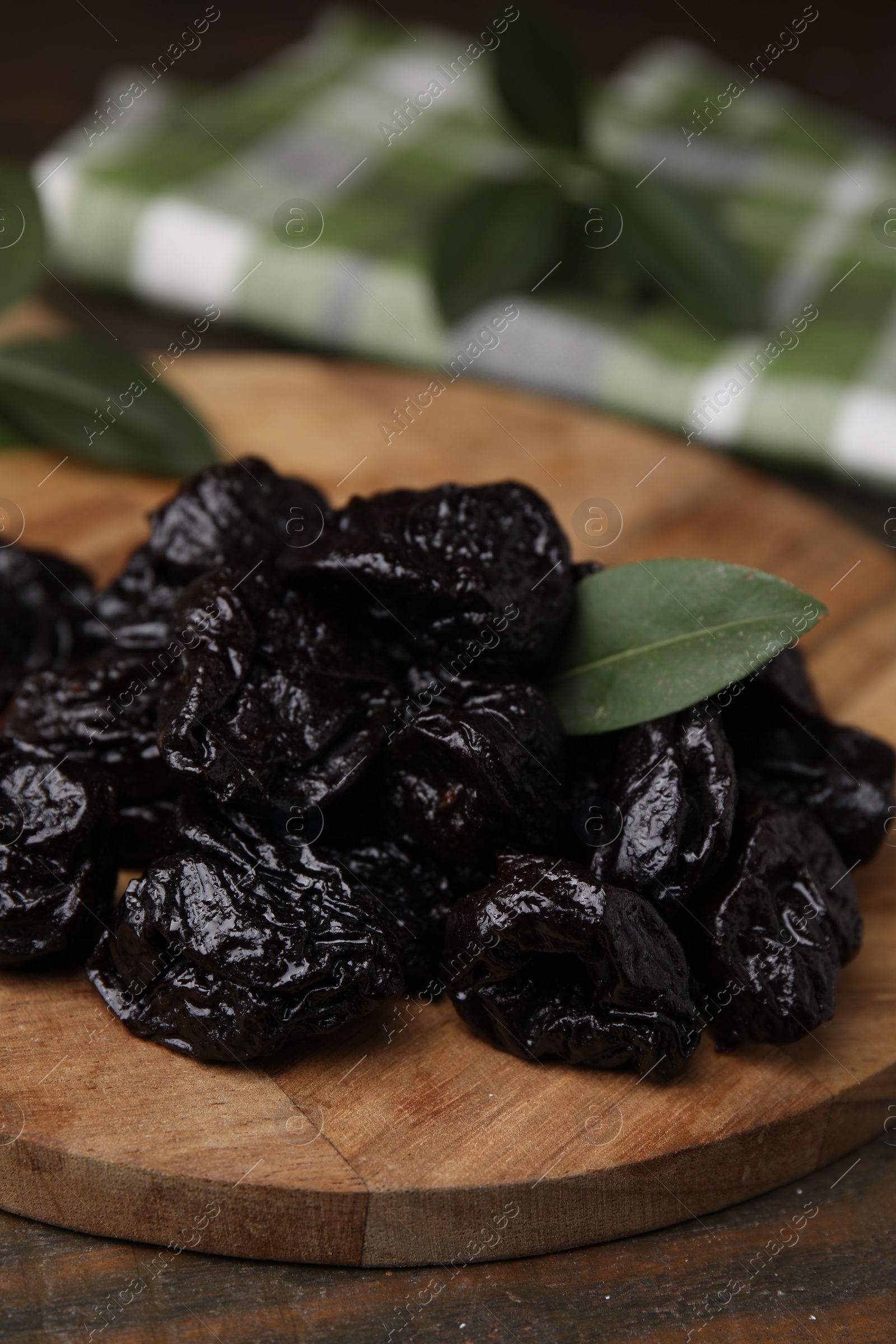 Photo of Tasty dried prunes and green leaf on wooden table, closeup