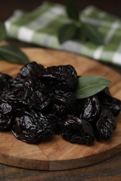 Photo of Tasty dried prunes and green leaf on wooden table, closeup