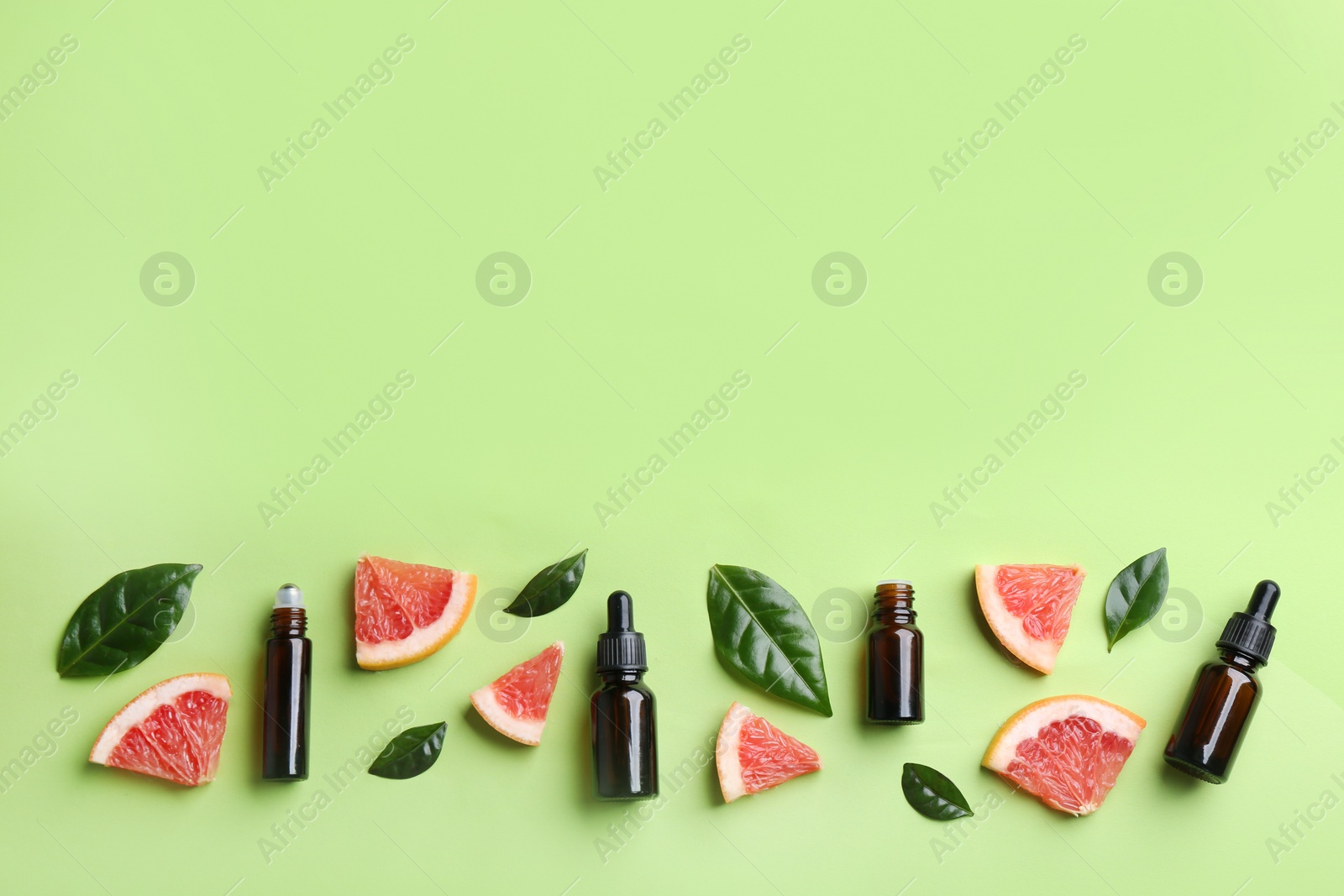 Photo of Flat lay composition with bottles of grapefruit essential oil on green background. Space for text