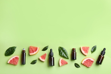 Flat lay composition with bottles of grapefruit essential oil on green background. Space for text