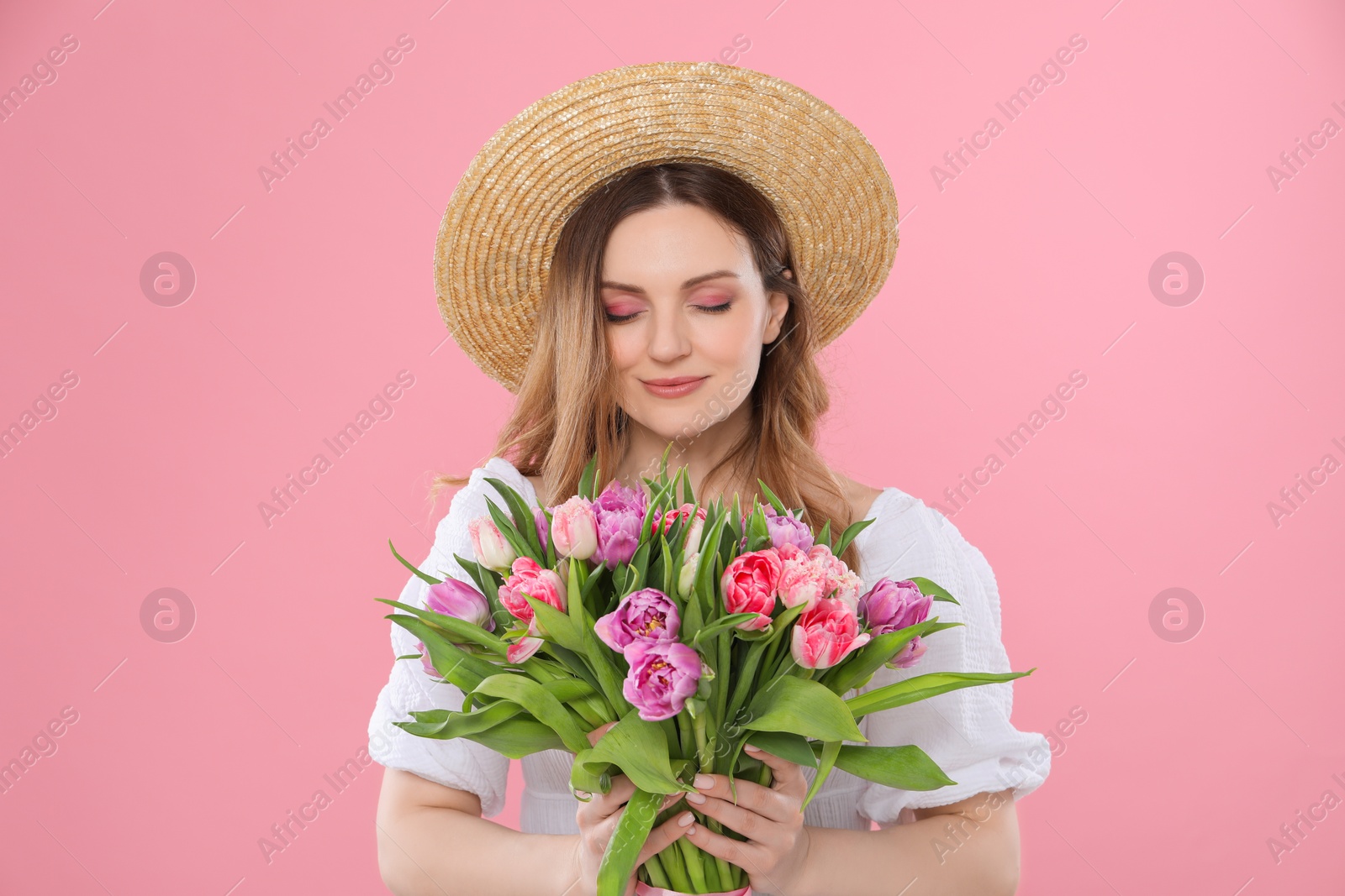 Photo of Happy young woman in straw hat holding bouquet of beautiful tulips on pink background