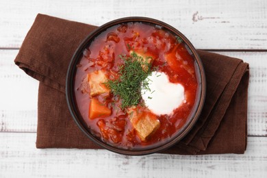 Tasty borscht with sour cream in bowl on white wooden table, top view