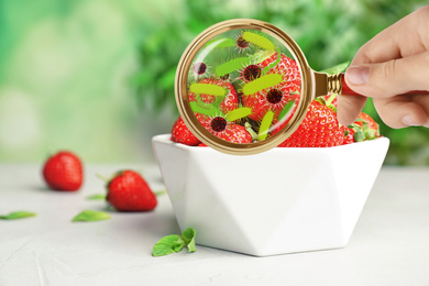 Image of Woman with magnifying glass detecting microbes on strawberries, closeup. Food poisoning concept  