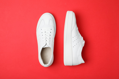 Stylish white shoes on red background, flat lay