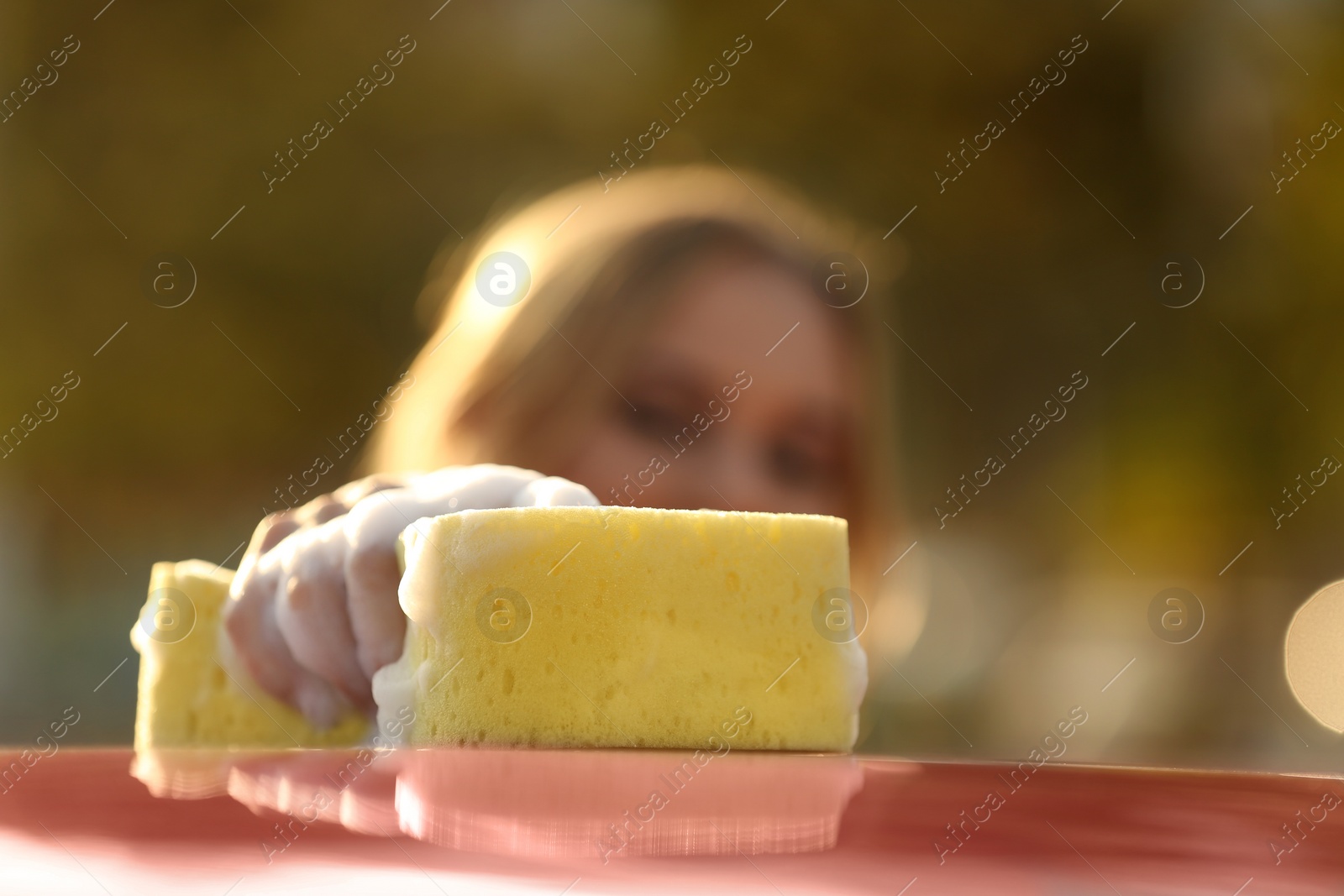 Photo of Young woman washing car outdoors, focus on sponge
