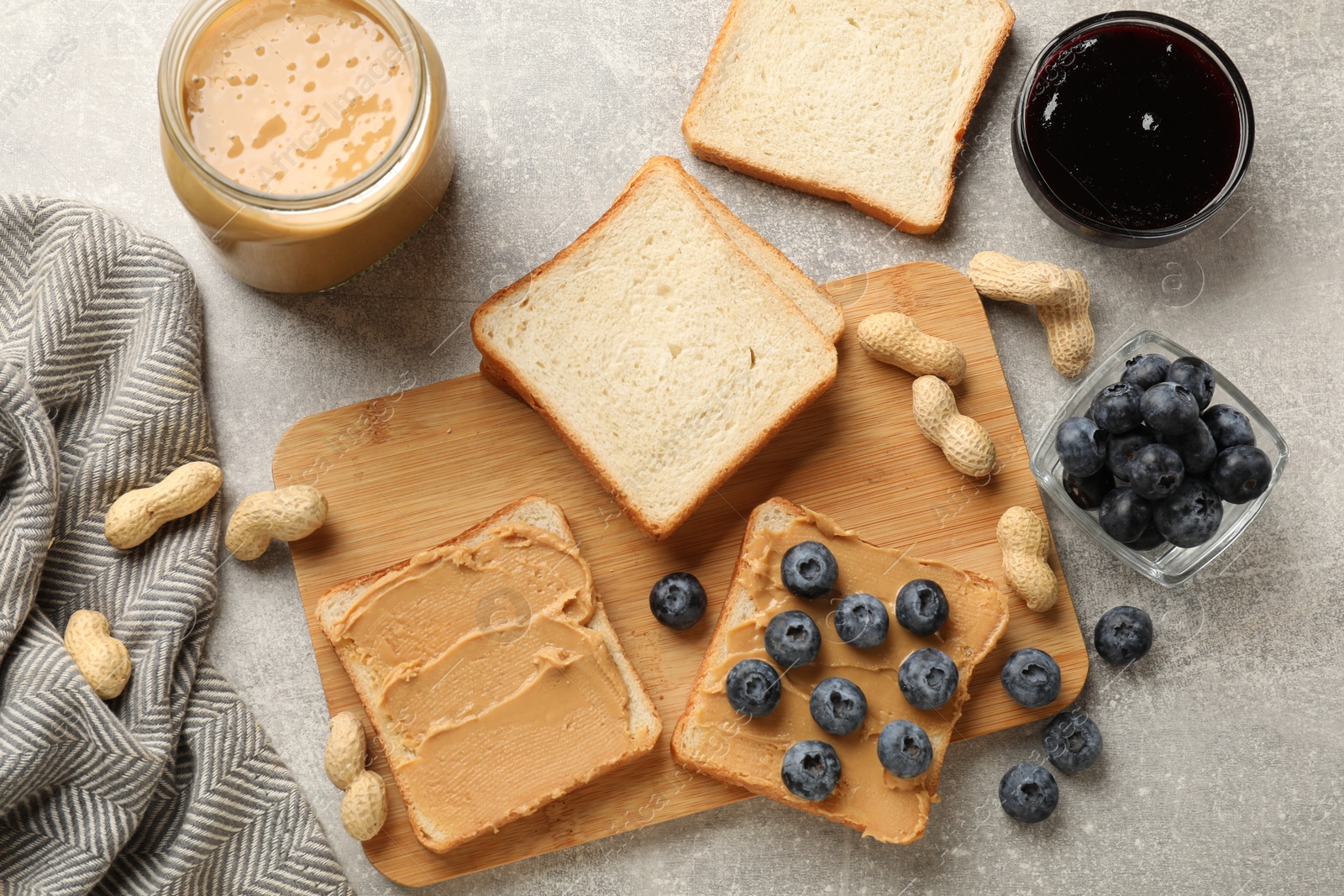 Photo of Tasty peanut butter sandwiches with fresh blueberries and jam on gray table, flat lay