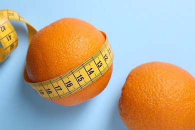 Photo of Cellulite problem. Orange with measuring tape near citrus on light blue background, flat lay