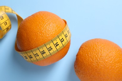 Cellulite problem. Orange with measuring tape near citrus on light blue background, flat lay