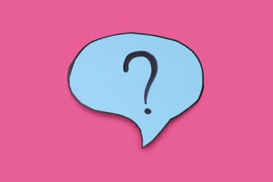 Photo of Paper speech bubble with question mark on pink background, top view