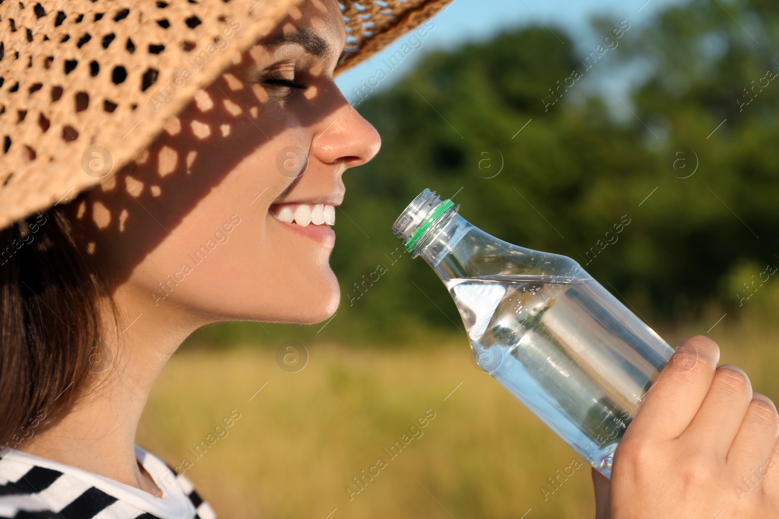 Photo of Happy woman in straw hat drinking water outdoors on hot summer day, closeup. Refreshing drink