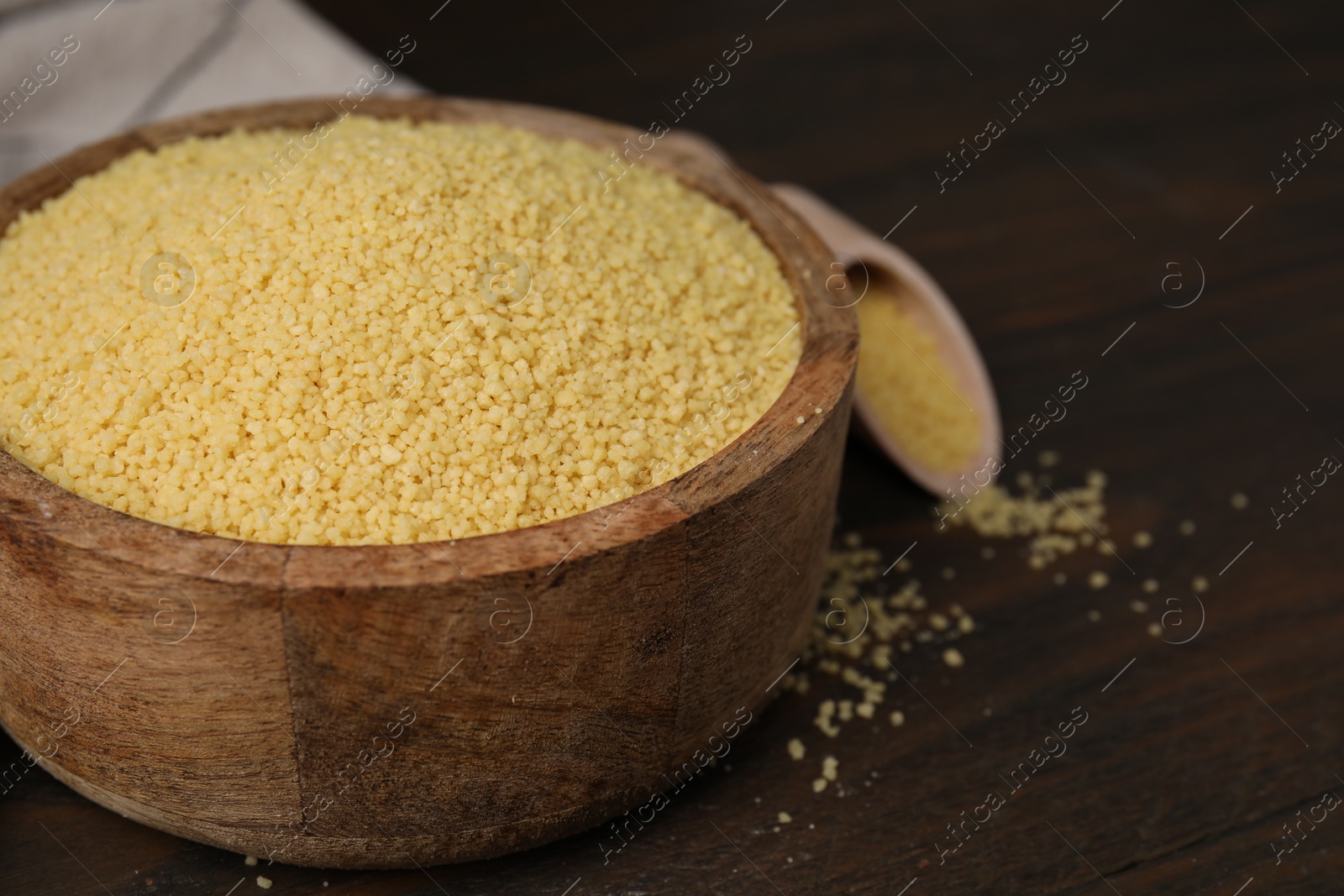 Photo of Raw couscous in bowl on wooden table, closeup