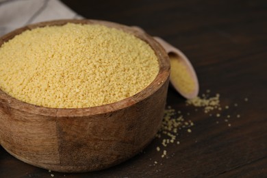 Photo of Raw couscous in bowl on wooden table, closeup