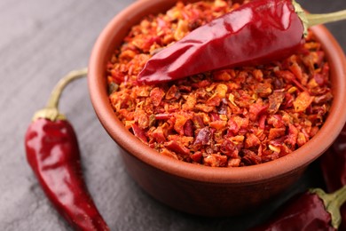 Photo of Chili pepper flakes in bowl and pods on dark textured table, closeup. Space for text