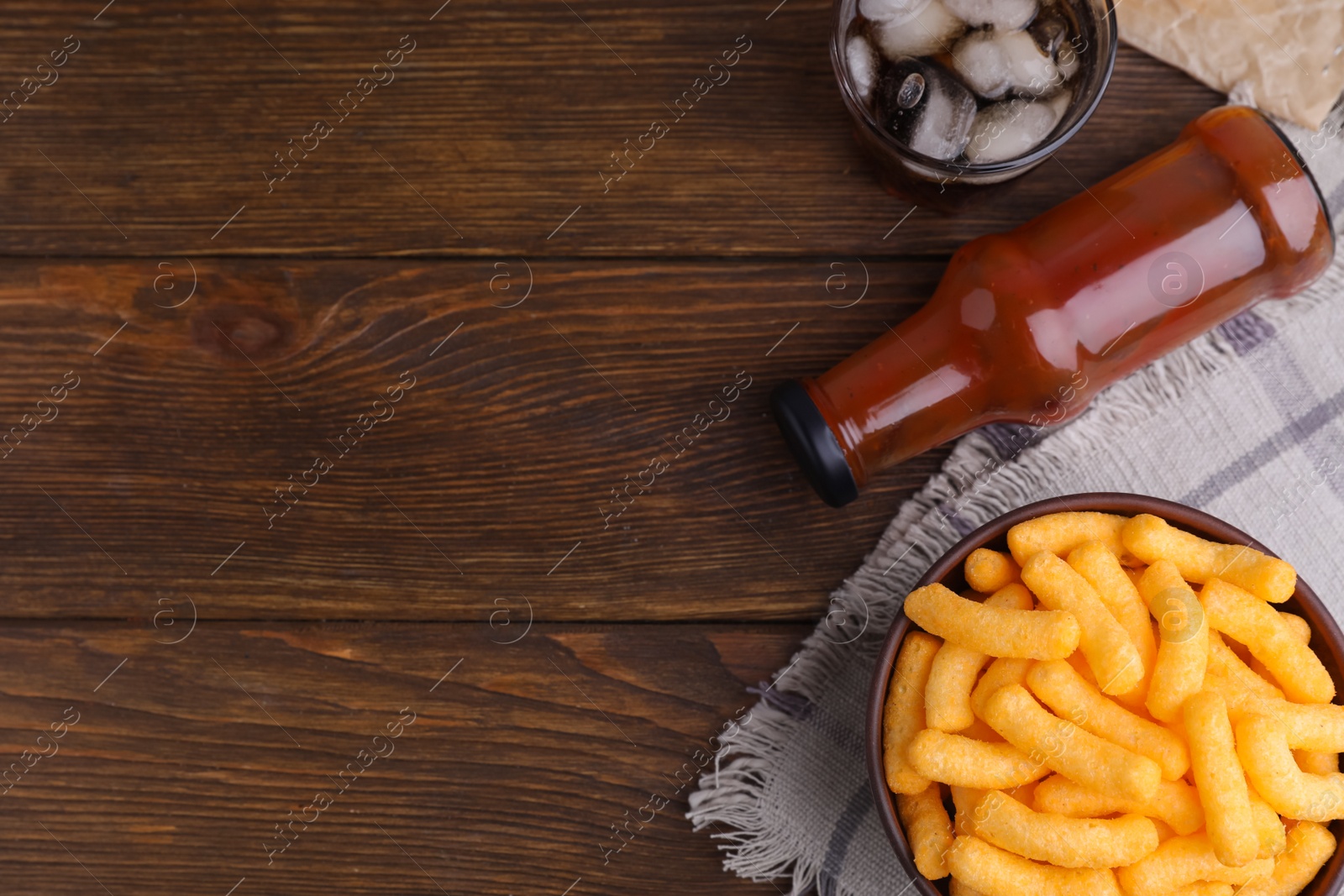 Photo of Crunchy cheesy corn snack, ketchup and refreshing drink on wooden table, flat lay. Space for text