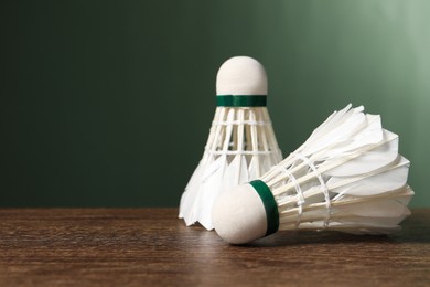 Photo of Feather badminton shuttlecocks on wooden table against green background, closeup. Space for text