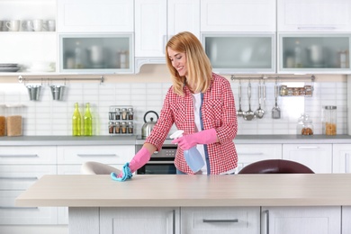 Photo of Woman cleaning table with rag in kitchen