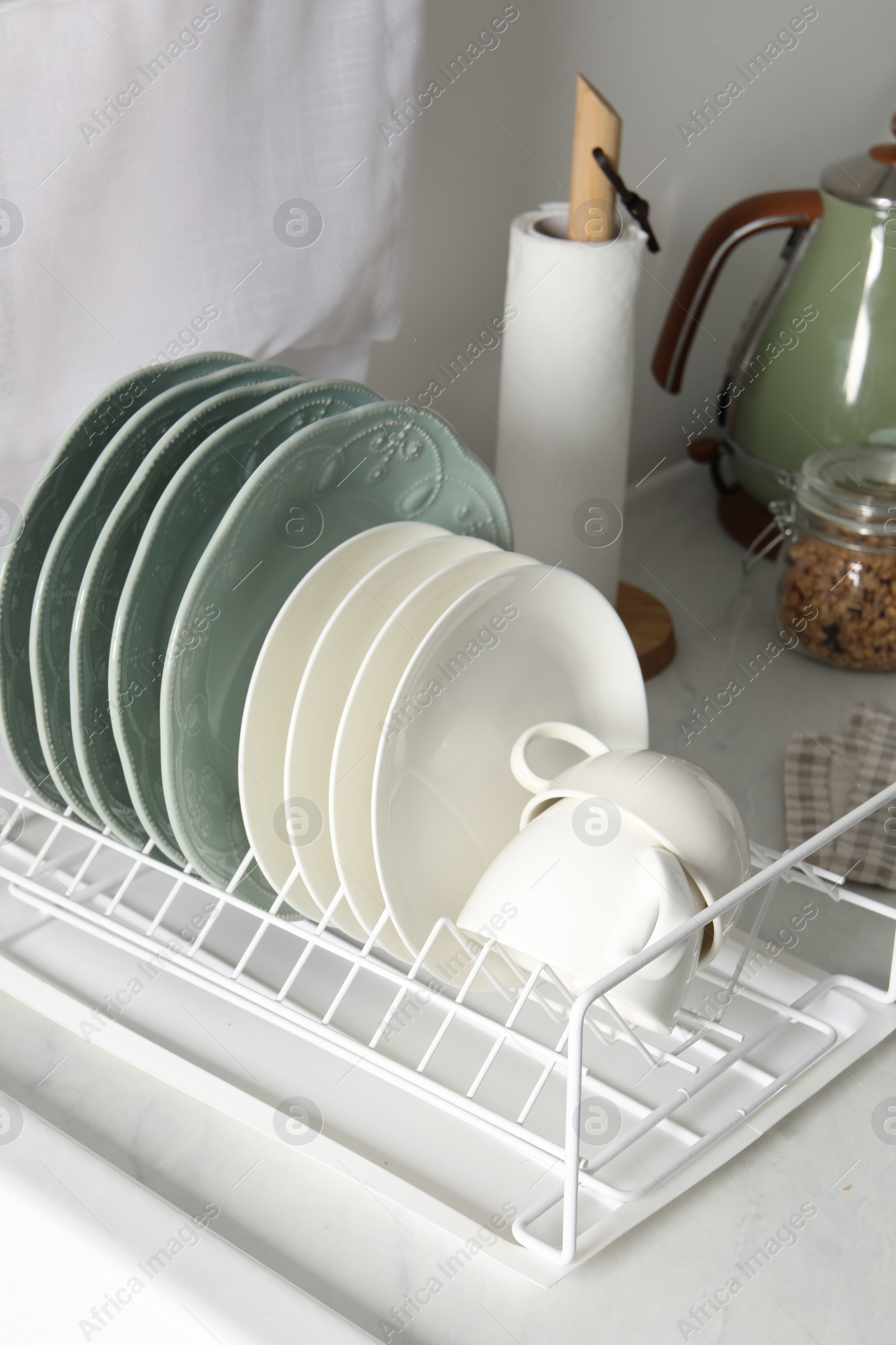 Photo of Drainer with different clean dishware and cups on white table in kitchen