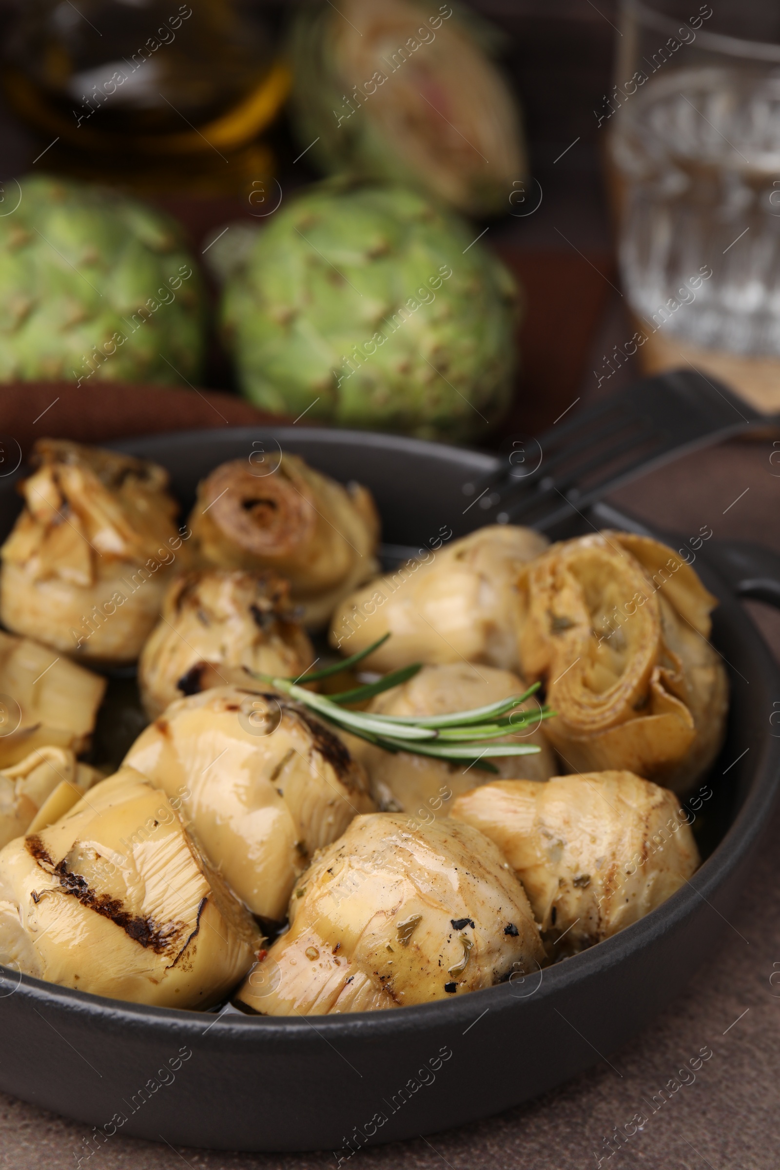 Photo of Delicious pickled artichokes with rosemary served on brown table, closeup