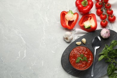 Delicious adjika sauce in bowl and ingredients on light marble table, flat lay. Space for text