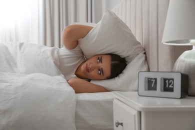 Photo of Unhappy young woman covering ears with pillow in bed at home. Noisy neighbours