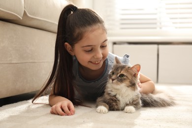 Photo of Cute little girl with cat lying on carpet at home. First pet