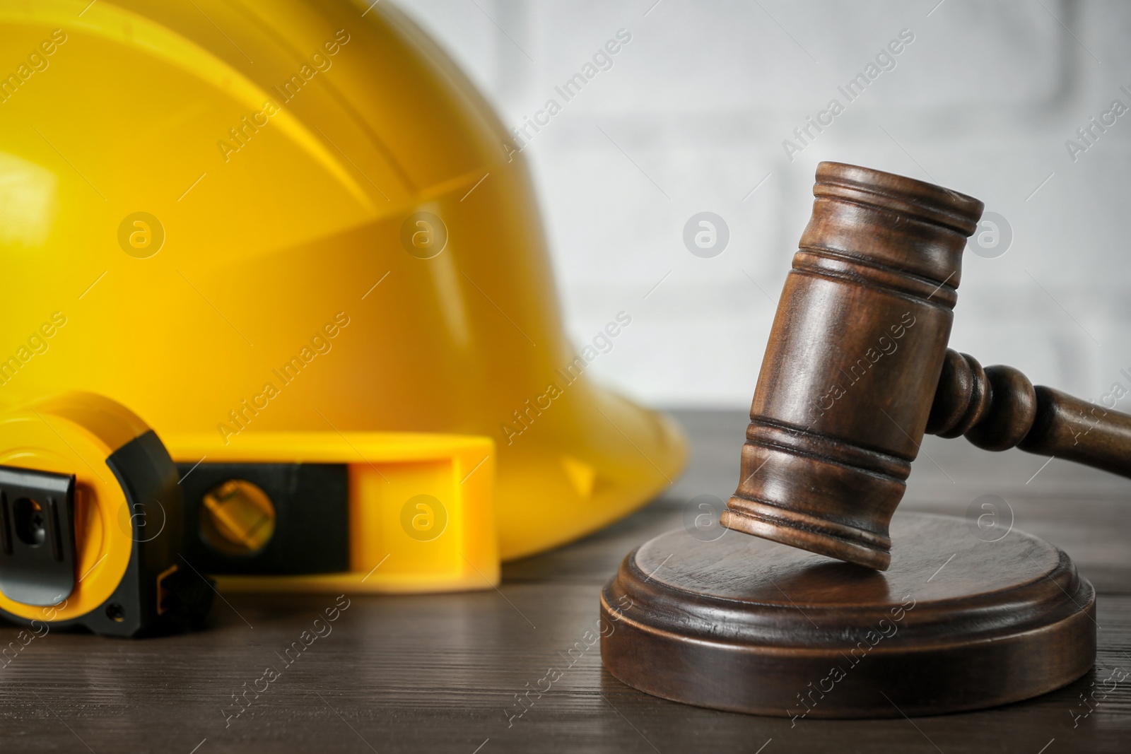 Photo of Construction and land law concepts. Judge gavel, protective helmet, level and tape measure on wooden table, closeup with space for text