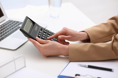 Photo of Woman using calculator at table indoors, closeup